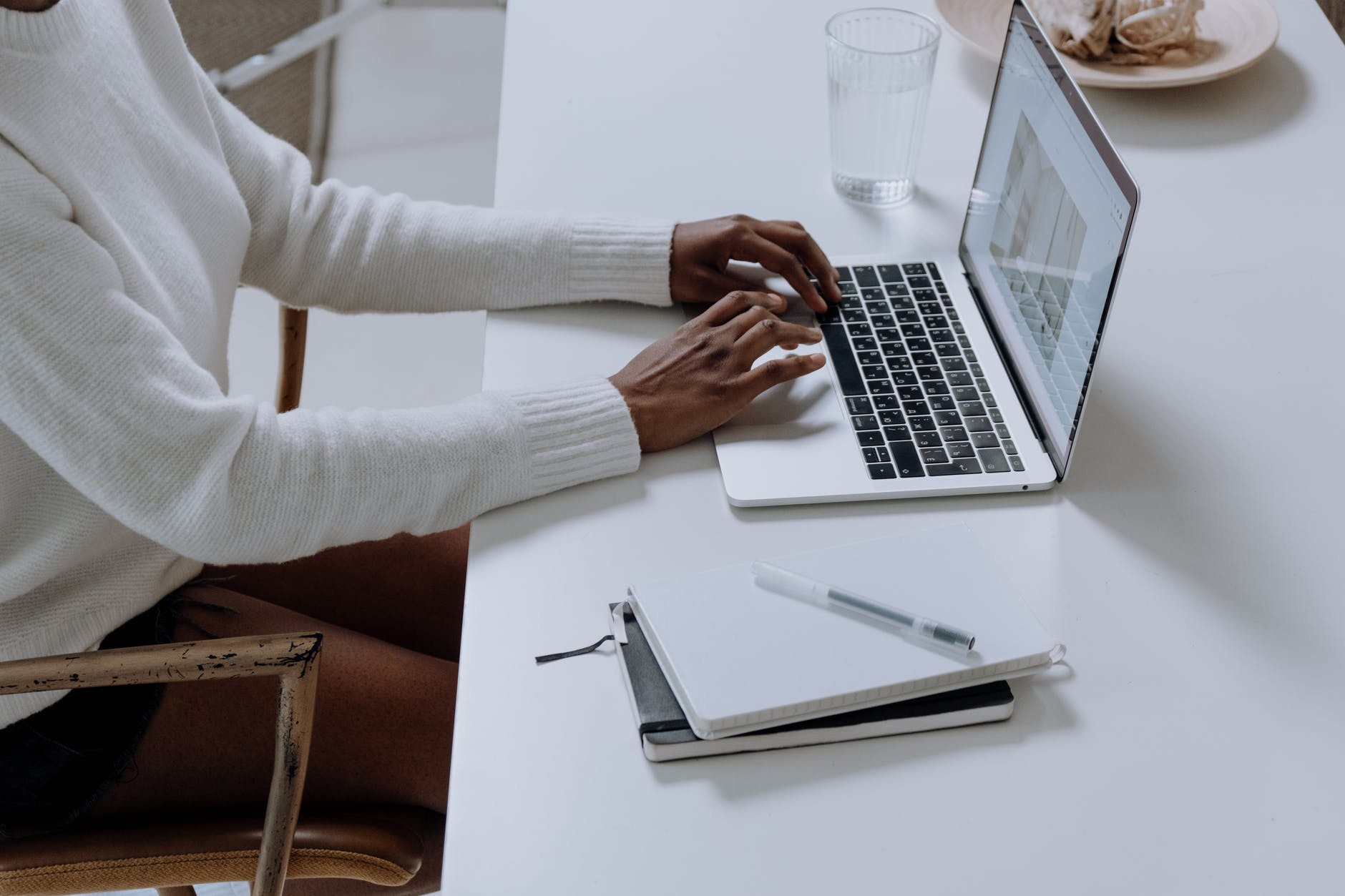 Person using a laptop, with notebooks and a pen.